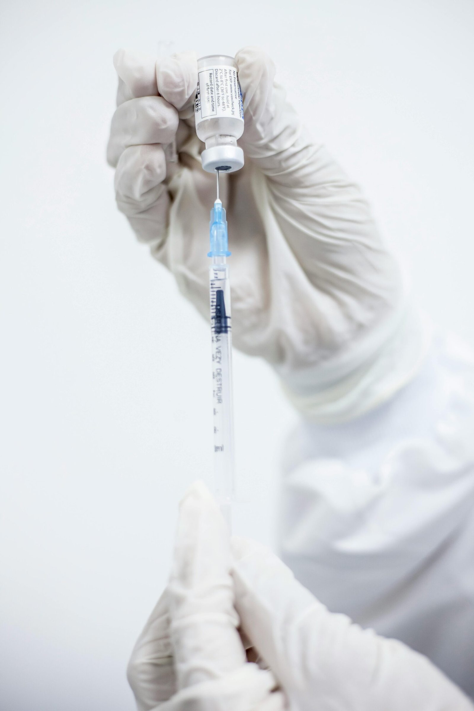 Close-up of medical professional's hands preparing a vaccine with syringe and vial.
