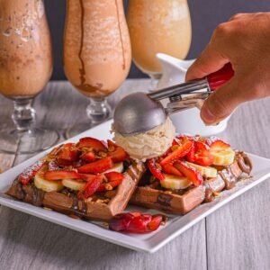 Indulgent waffles topped with bananas, strawberries, and ice cream, served indoors with milkshakes.