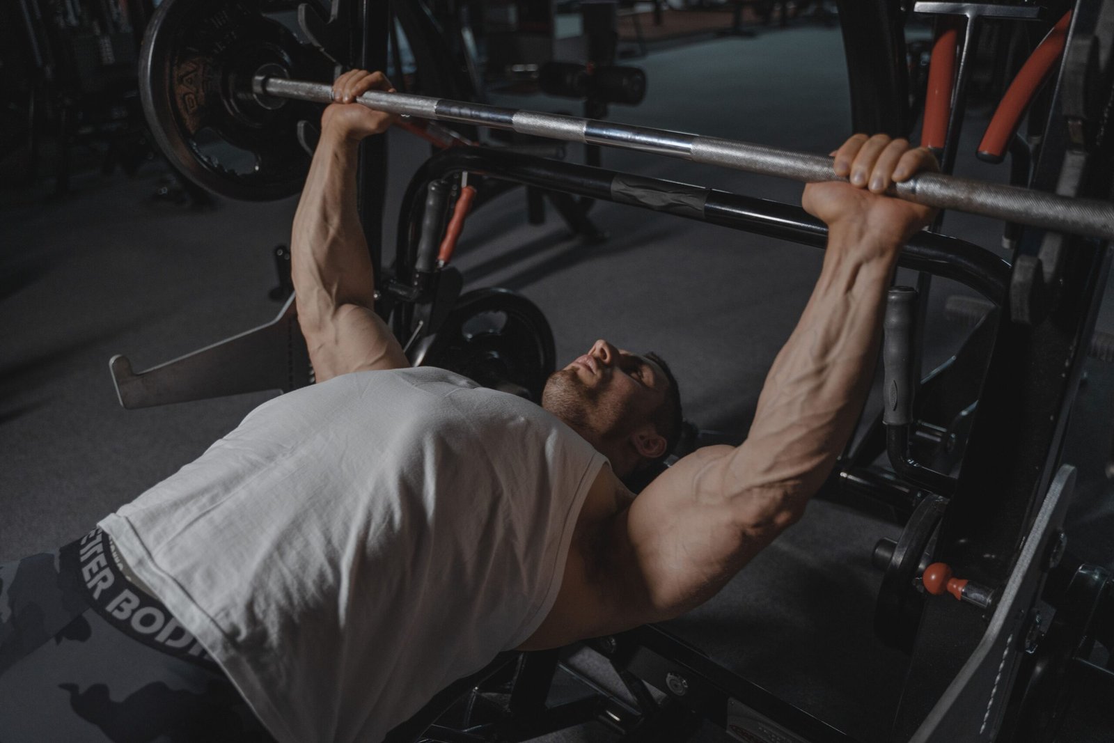 pexels photo 5327556 5327556 A focused man lifts heavy weights on a bench press machine in a dimly lit gym.