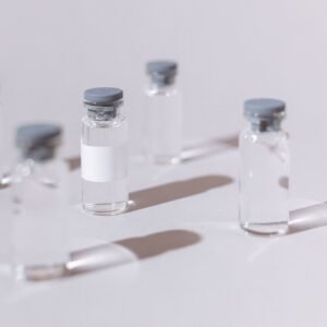 Clear glass vials used for vaccines or medication, displayed on a sterile white surface.