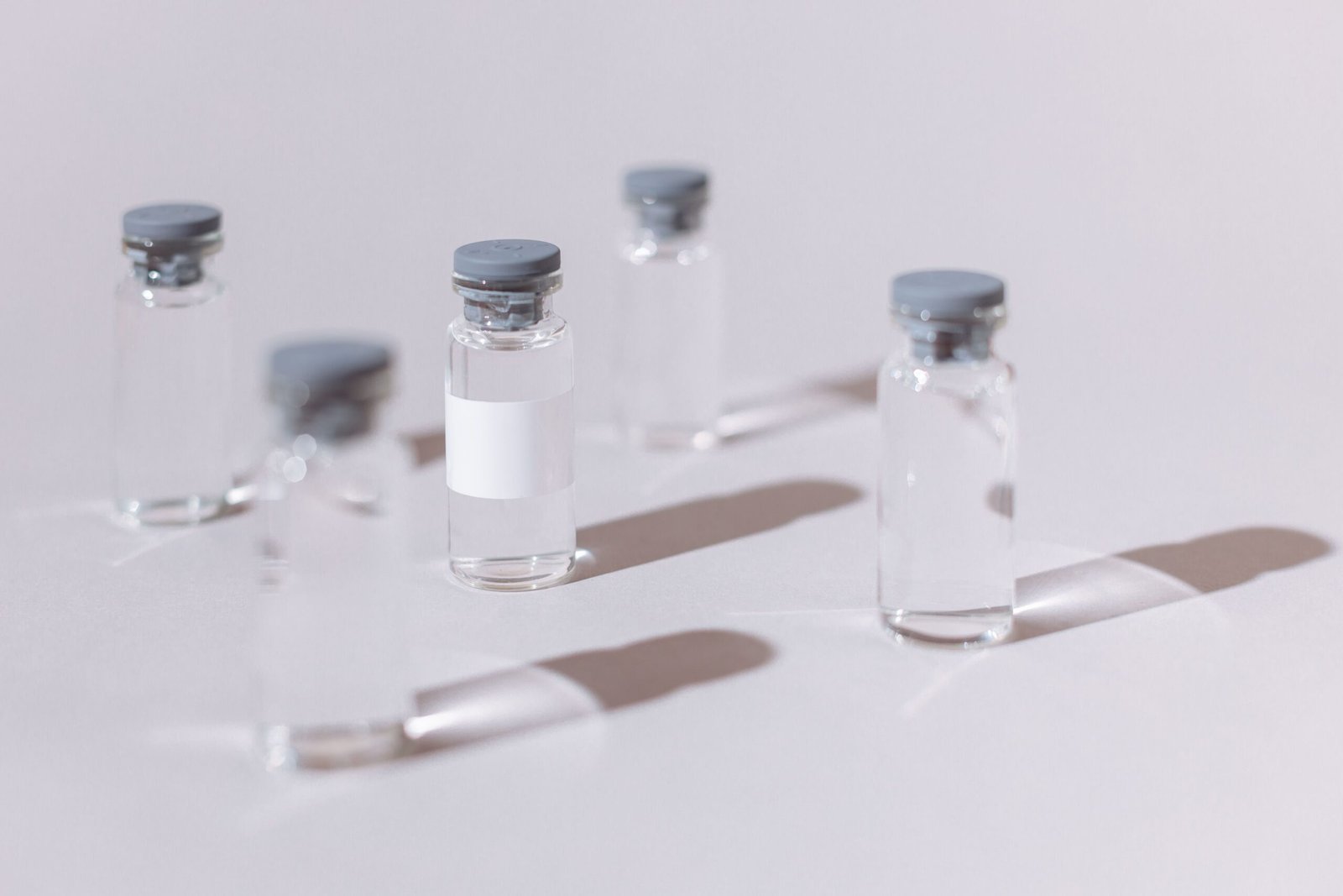 pexels photo 5922066 5922066 Clear glass vials used for vaccines or medication, displayed on a sterile white surface.