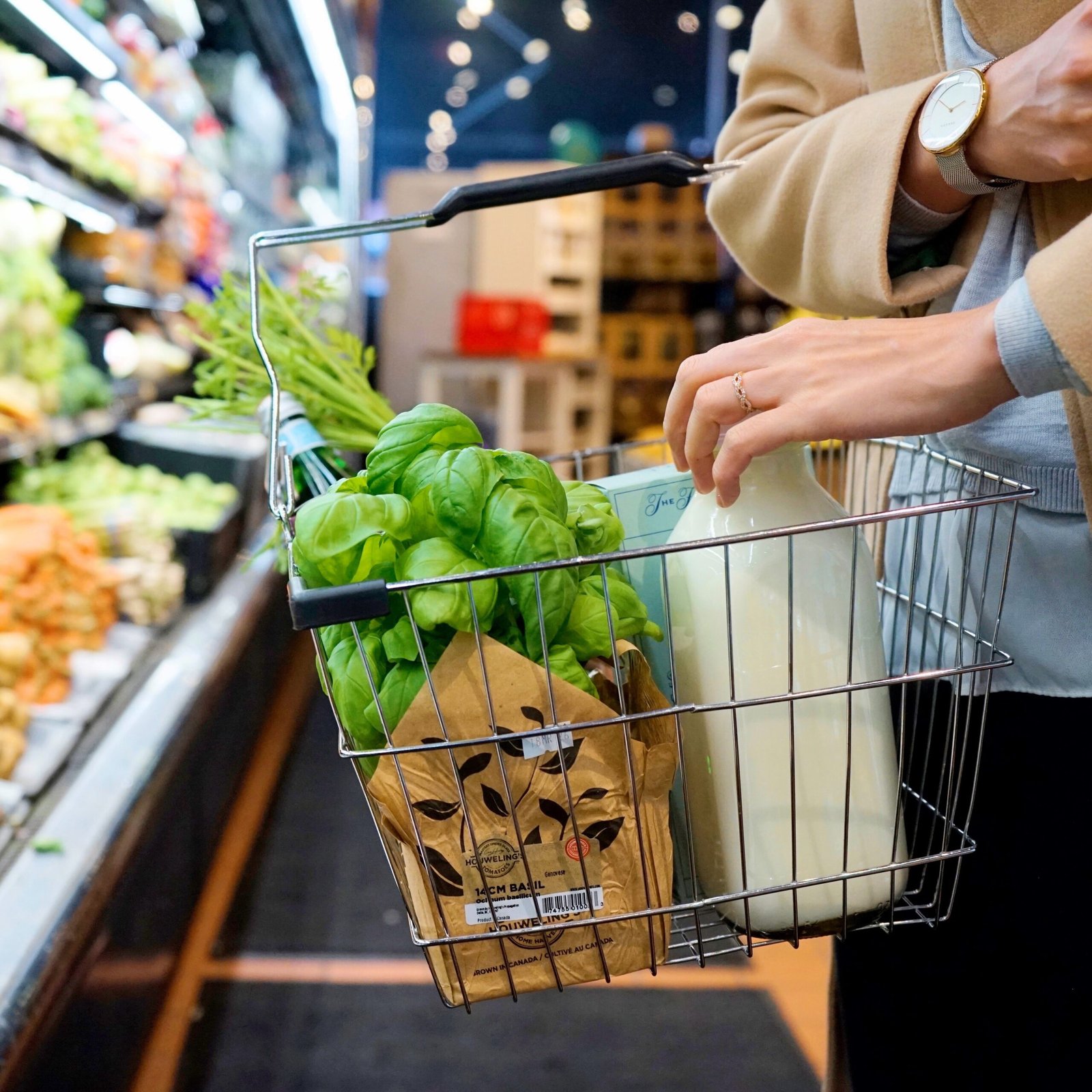 pexels photo 9070110 9070110 A person shops in a grocery store with a basket containing fresh greens, milk, and herbs.